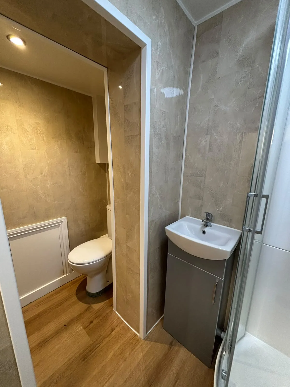 Bathroom with a toilet, small sink with cabinet, and a shower cabin.