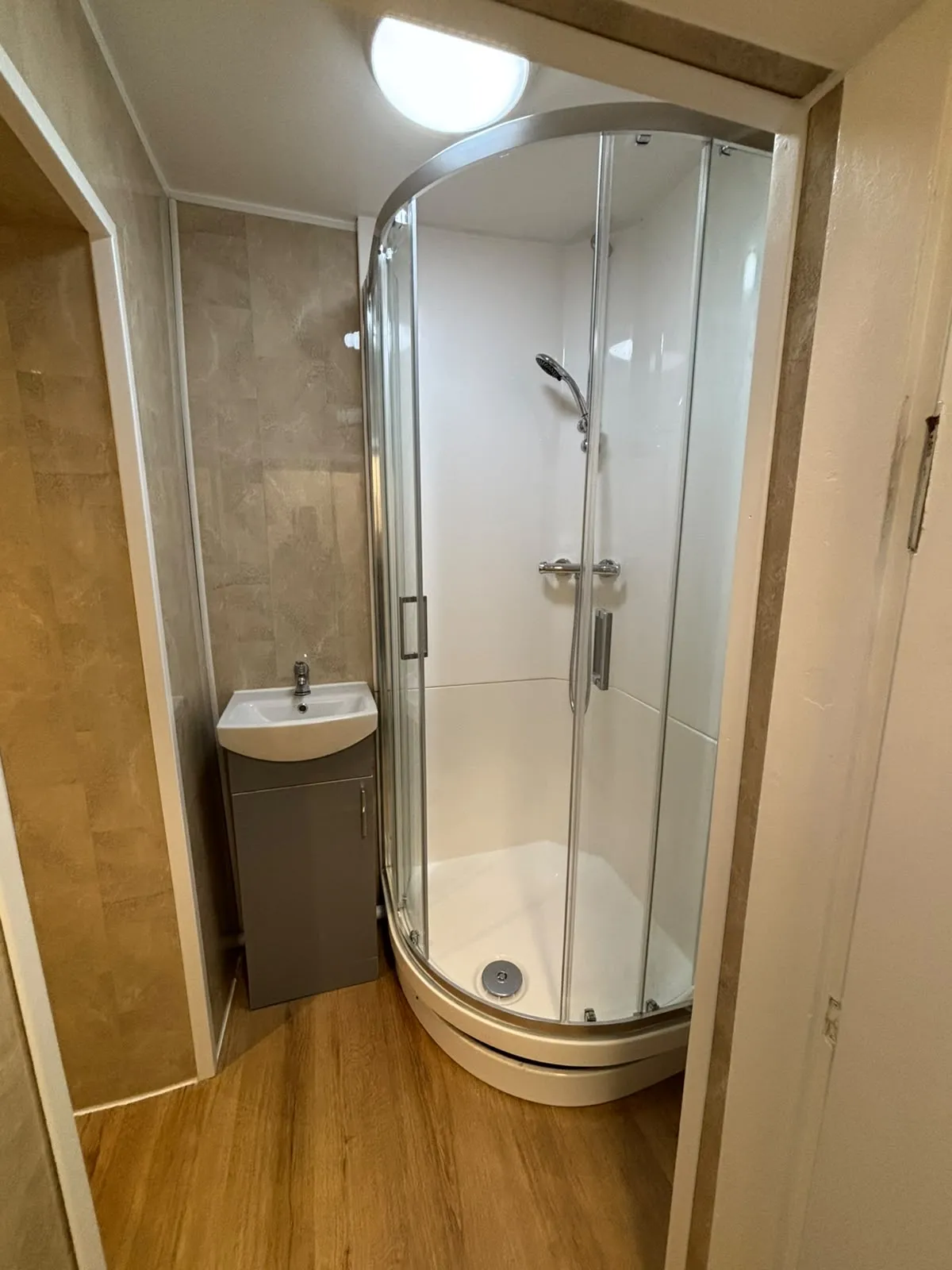 Small bathroom with a curved glass corner shower enclosure and a compact sink with a gray cabinet.
