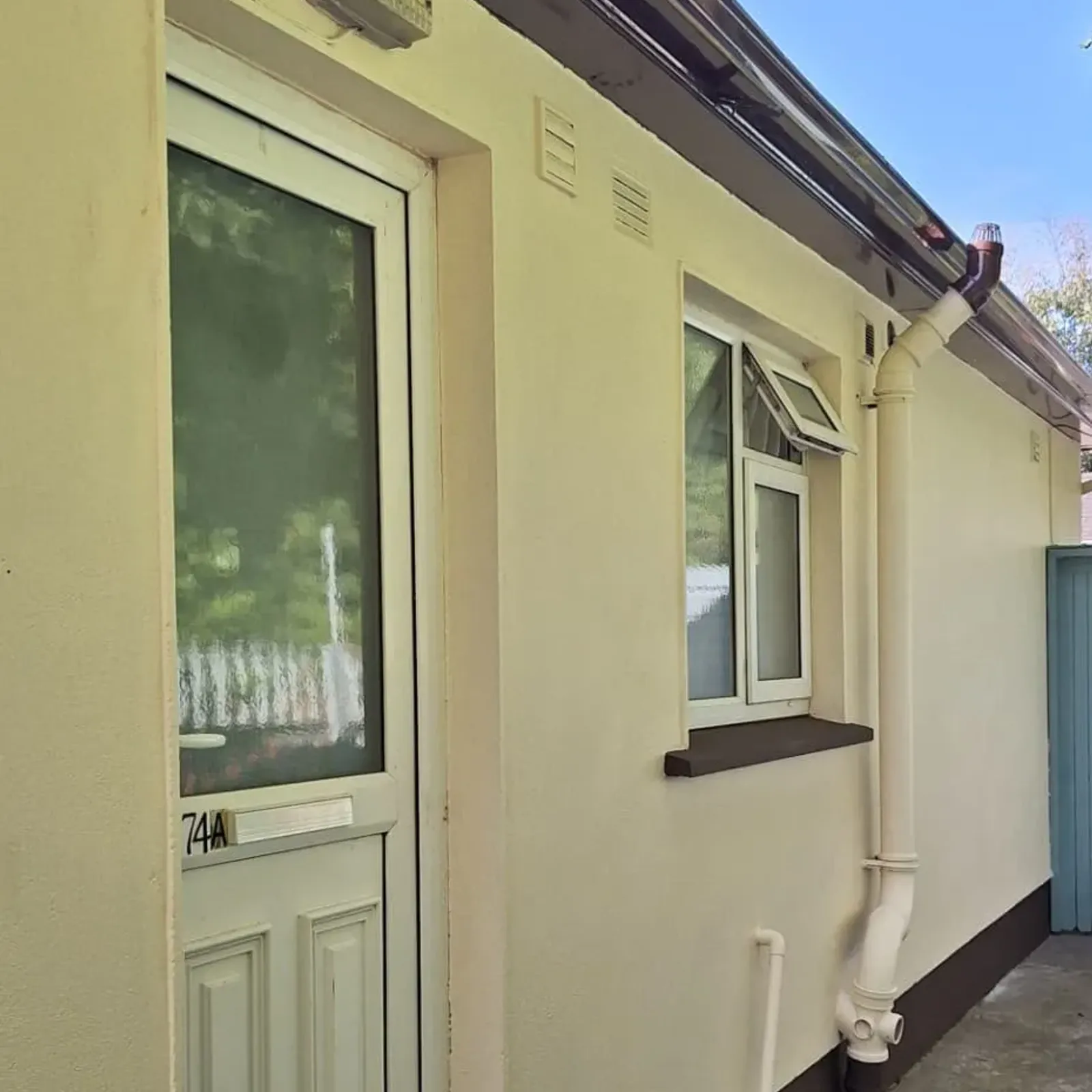 Exterior walkway with a white framed door and nearby small window on a light-colored wall, visible downspout and outdoor light above the door.