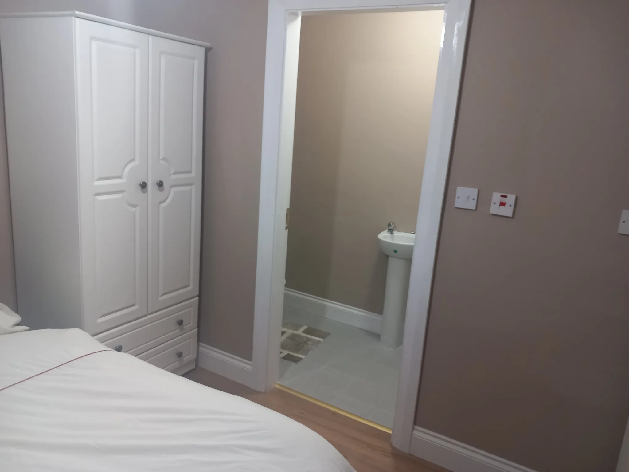 Bedroom with double bed and white wardrobe, adjoining ensuite bathroom with pedestal sink and mirror