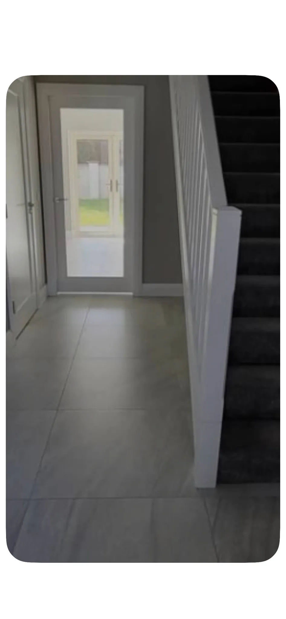 Hallway with tiled floor, a carpeted staircase on the right, and a glass door at the far end showing an outdoor area.