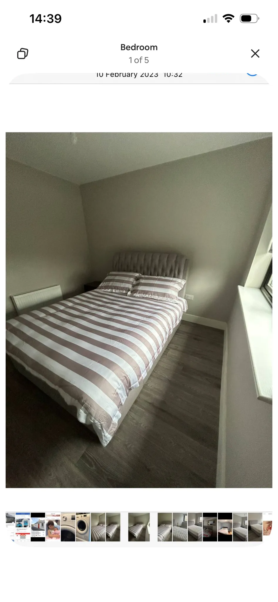 Bedroom with a double bed with striped duvet and two pillows, upholstered headboard, window on the right and a radiator on the left.