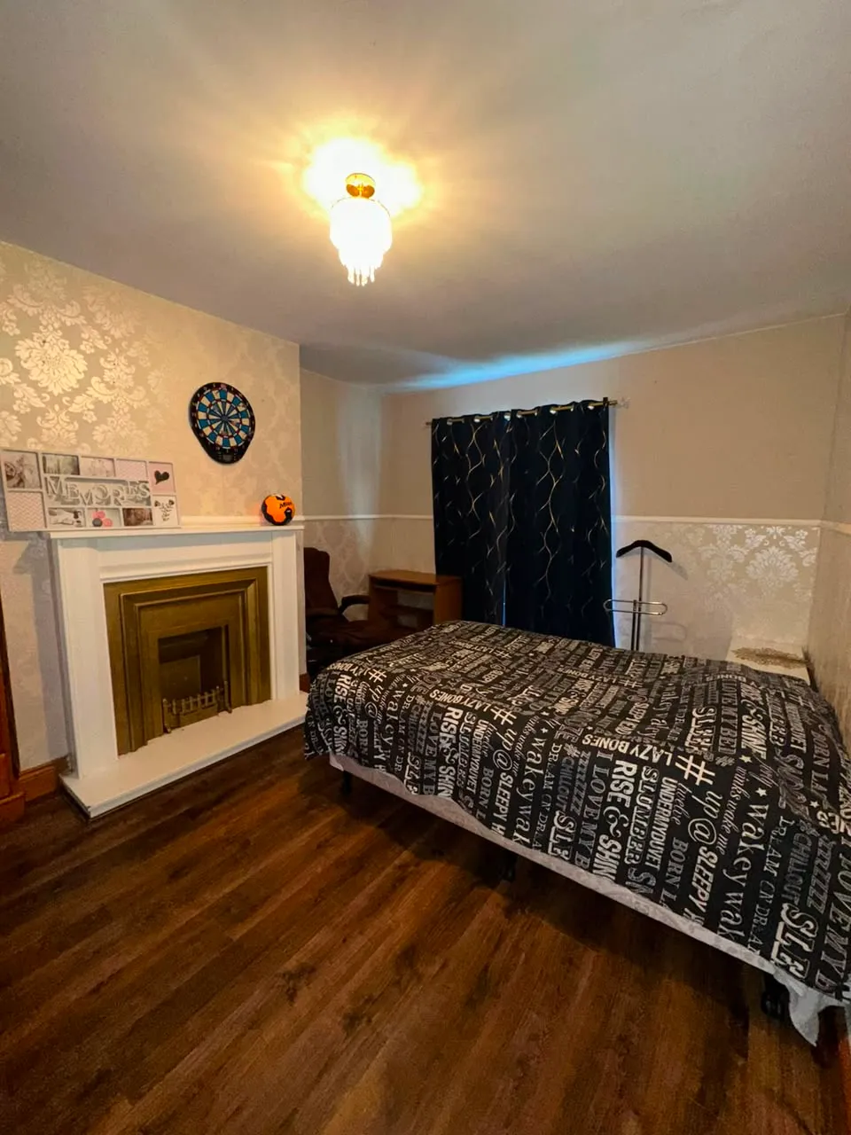 Bedroom with a double bed, fireplace, desk, chair and dark curtains over a window.