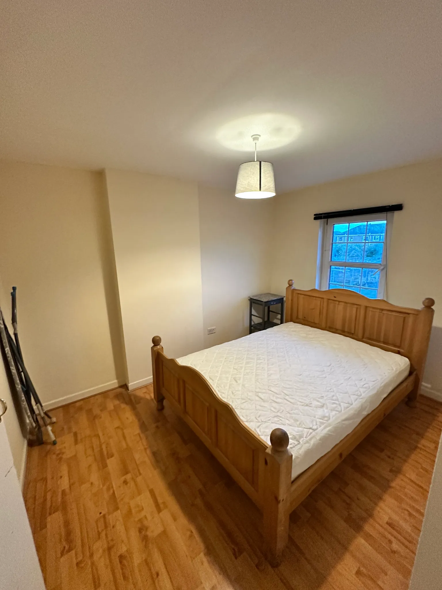 Bedroom with a wooden double bed, mattress, small bedside table, pendant ceiling light and a window.