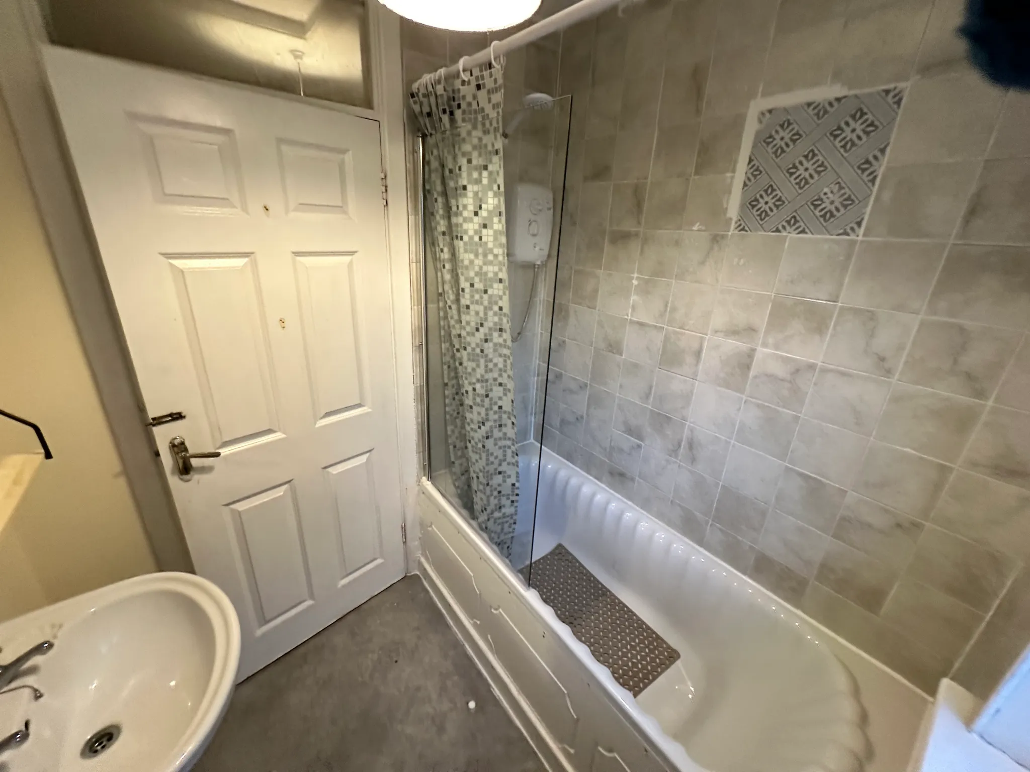 Bathroom with a bathtub and shower (shower curtain and glass screen), tiled walls, sink, and a closed door.