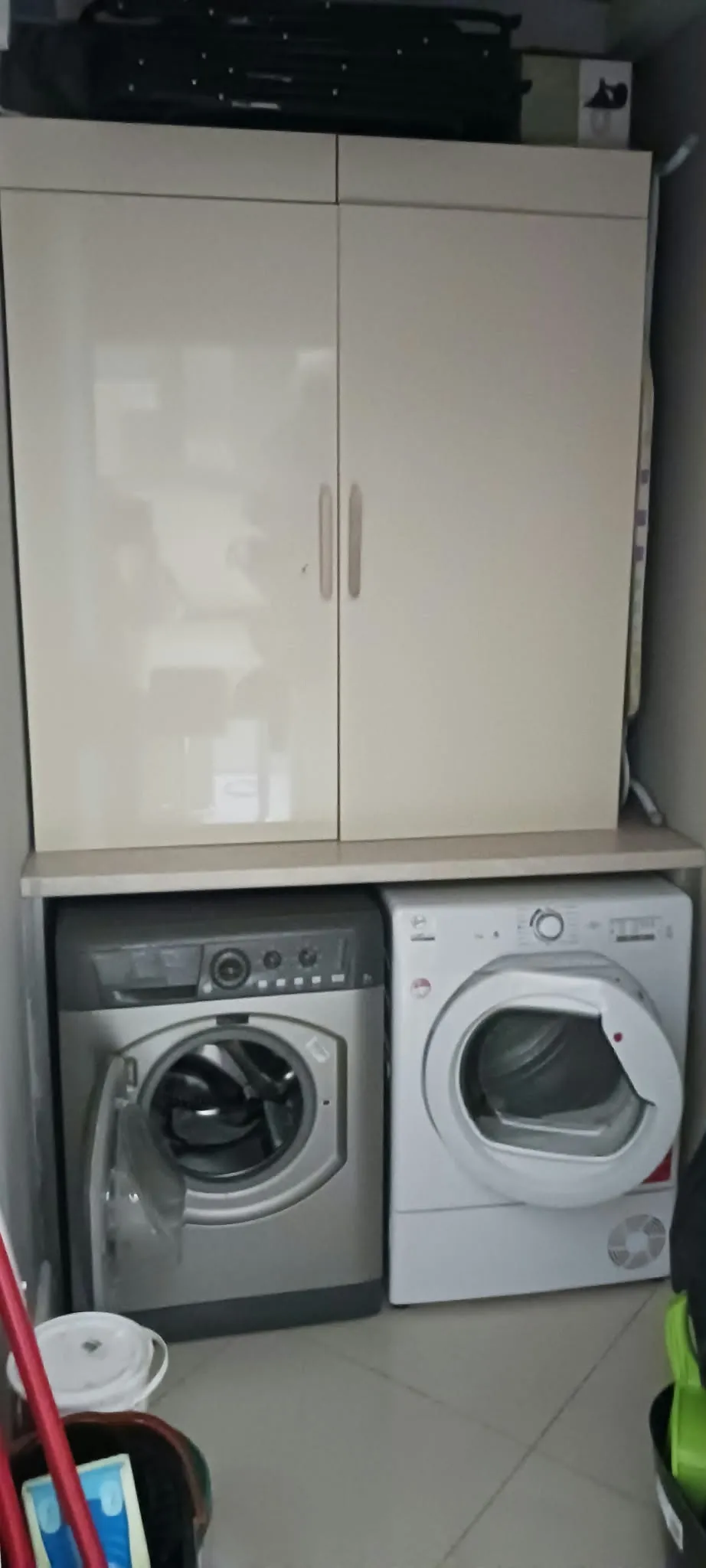 Laundry area with two front-loading machines side by side under a countertop and a two-door cabinet above.