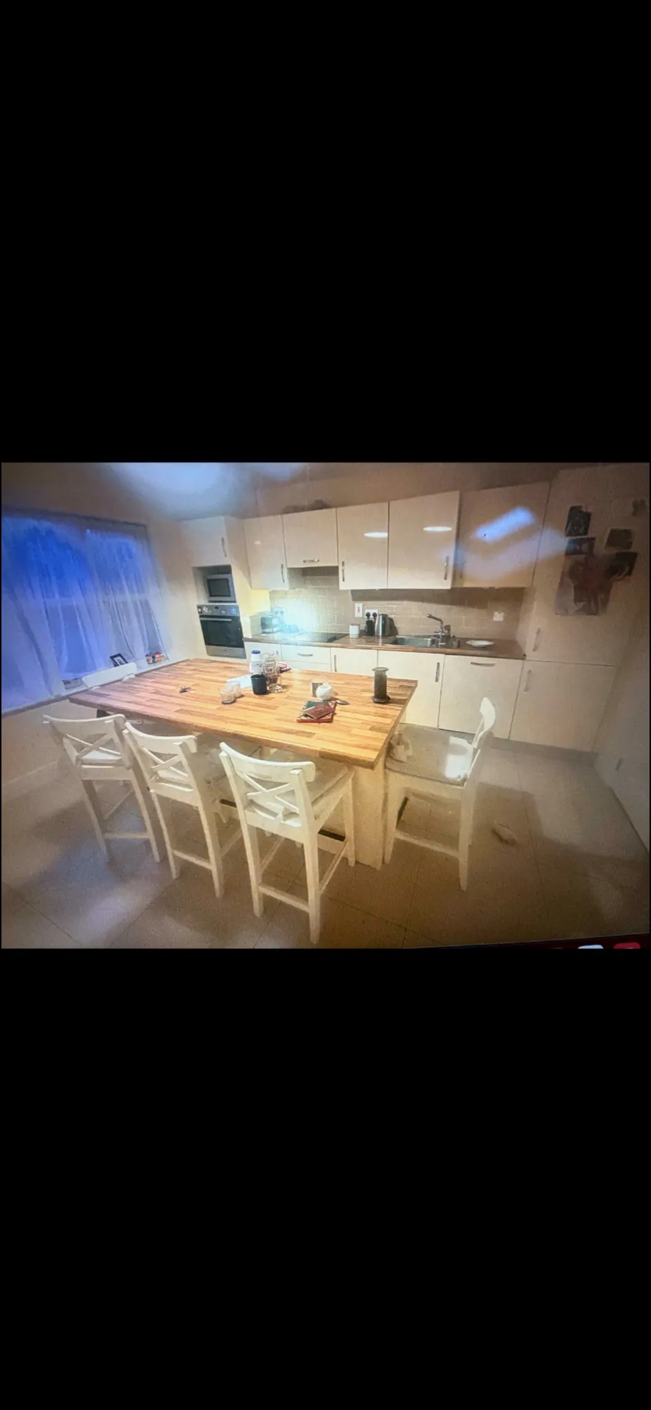Kitchen and dining area with cream cabinetry, wooden dining table with white chairs, window with blue curtains, and built-in appliances