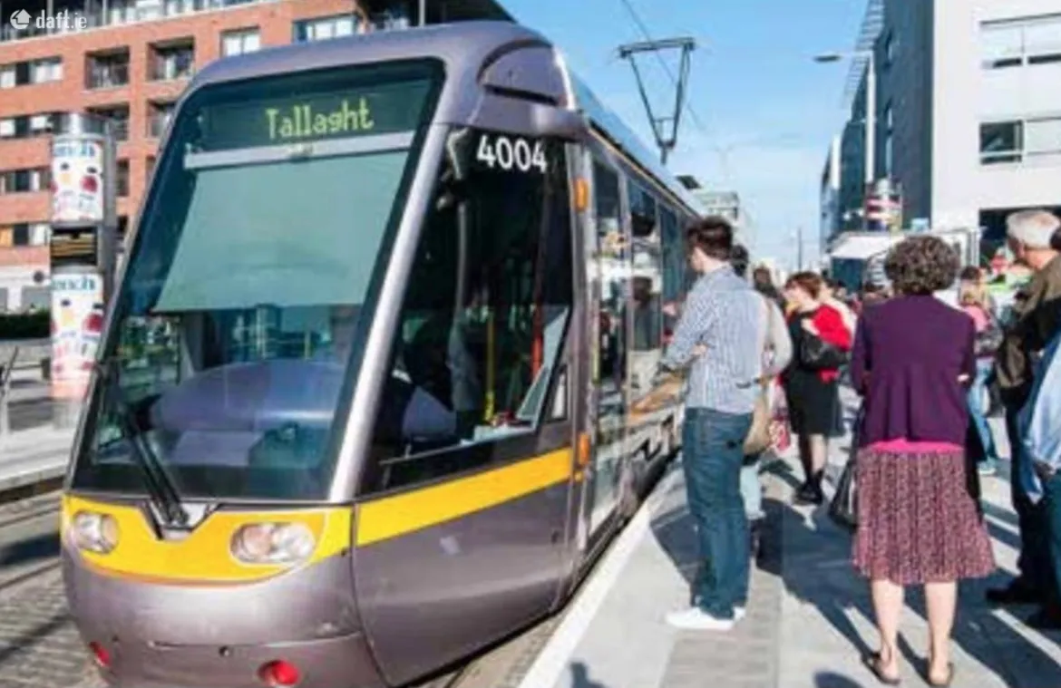 Exterior view of a tram at a street stop with several people waiting on the platform.