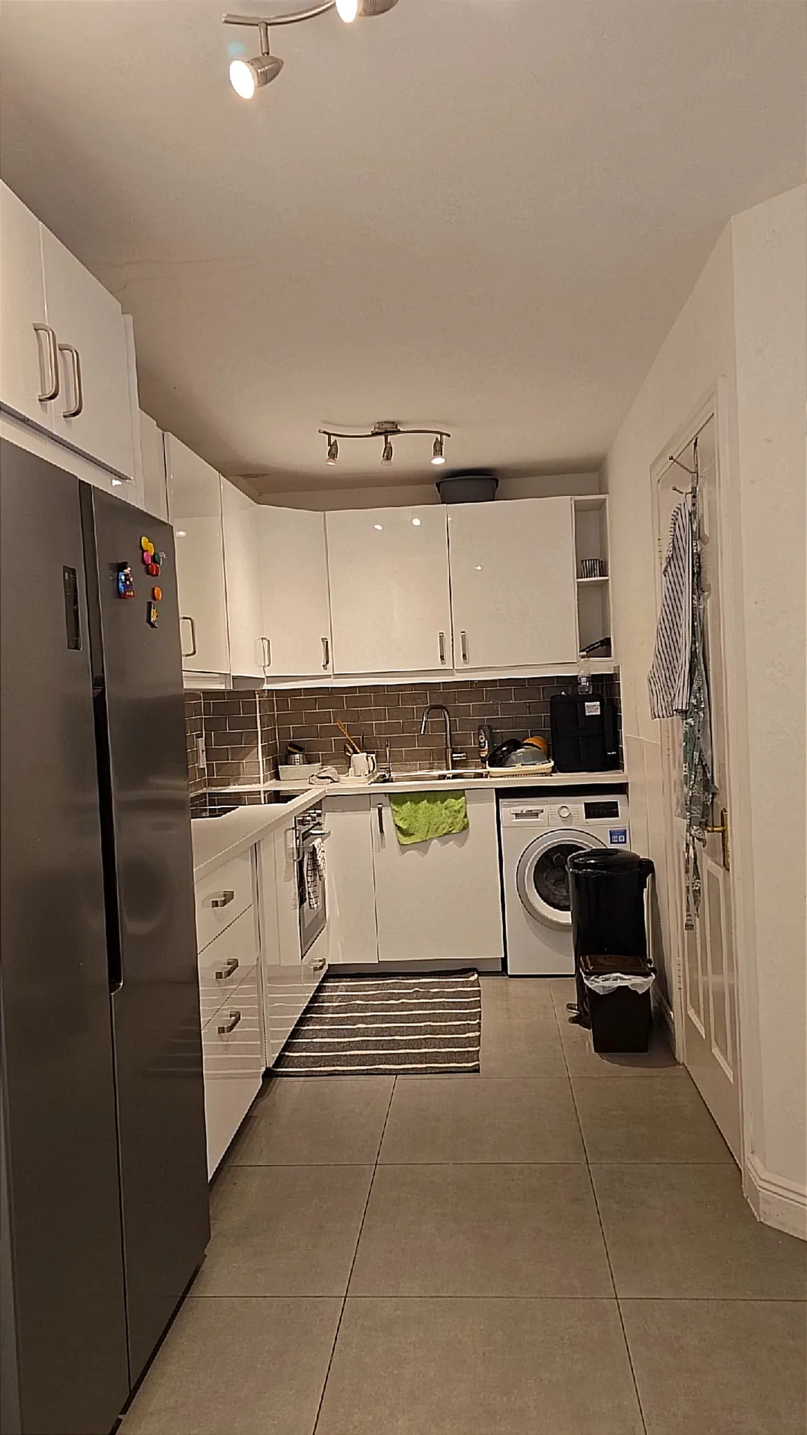 Kitchen with white cabinetry, stainless steel refrigerator, integrated oven, washing machine, brown subway tile backsplash, and tile flooring