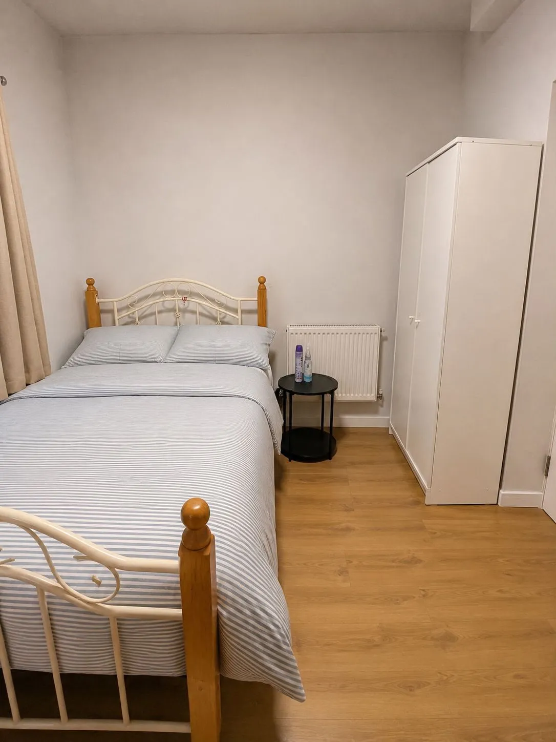 Bedroom with a double bed, small round bedside table, radiator and a freestanding white wardrobe