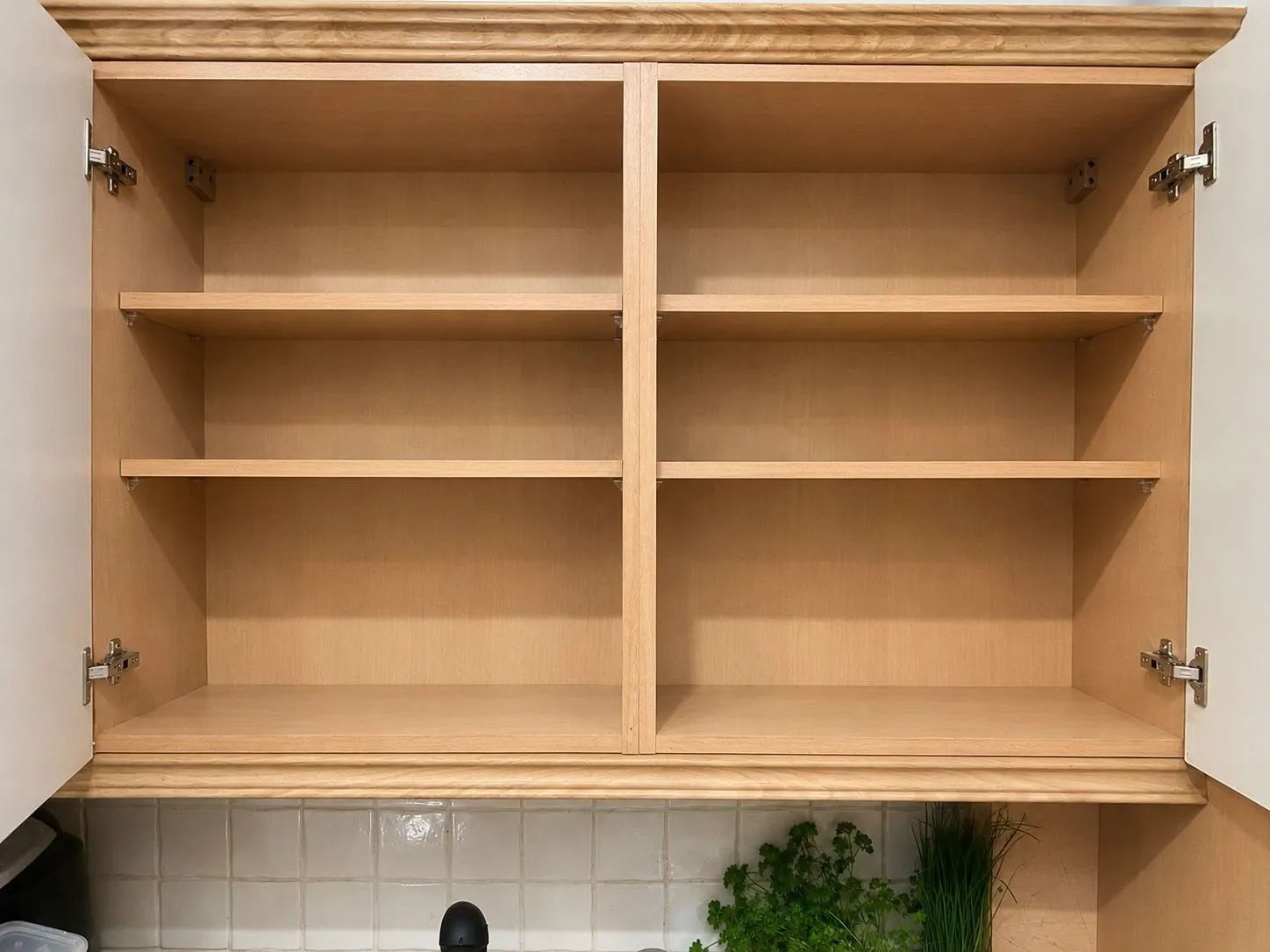 Open wooden kitchen cabinet with four shelves above a tiled backsplash and countertop