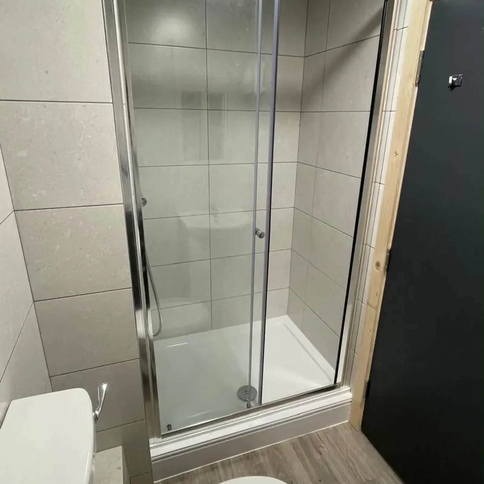 Bathroom with a corner shower with sliding glass doors, tiled walls, toilet, and wood-look floor.