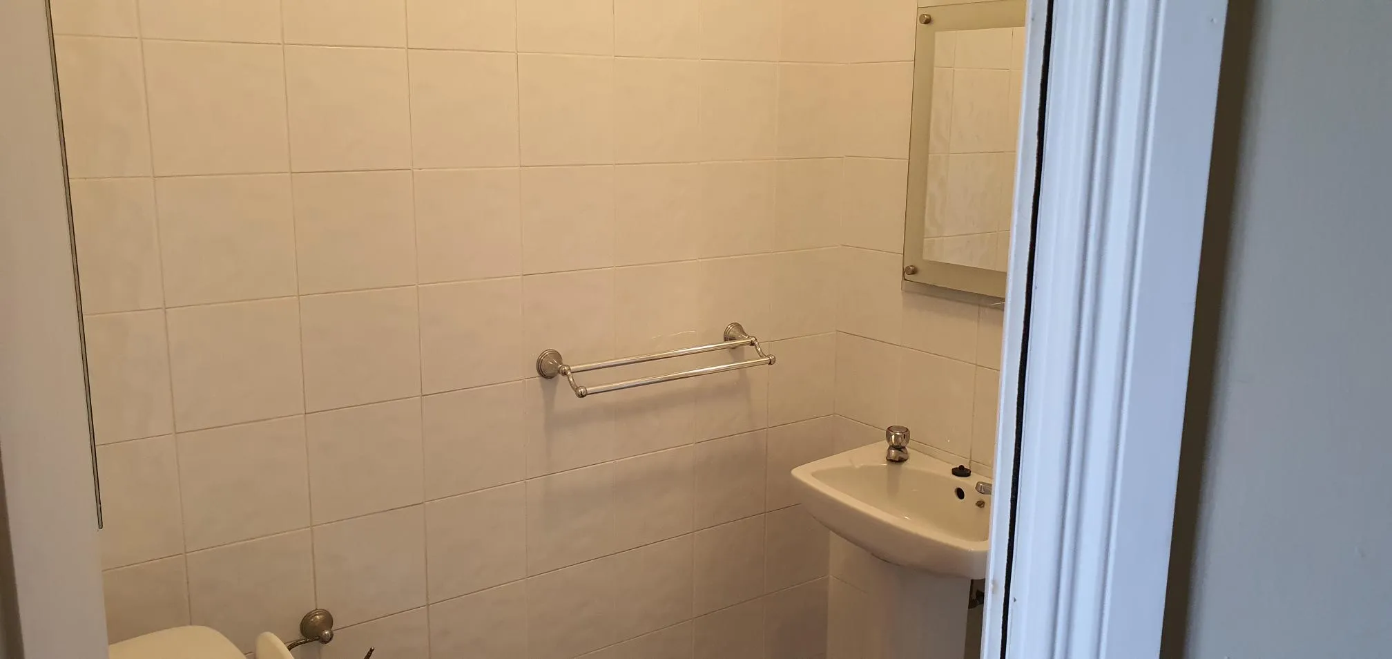 Bathroom with cream tile walls, pedestal sink, towel rack, and shower enclosure with glass door