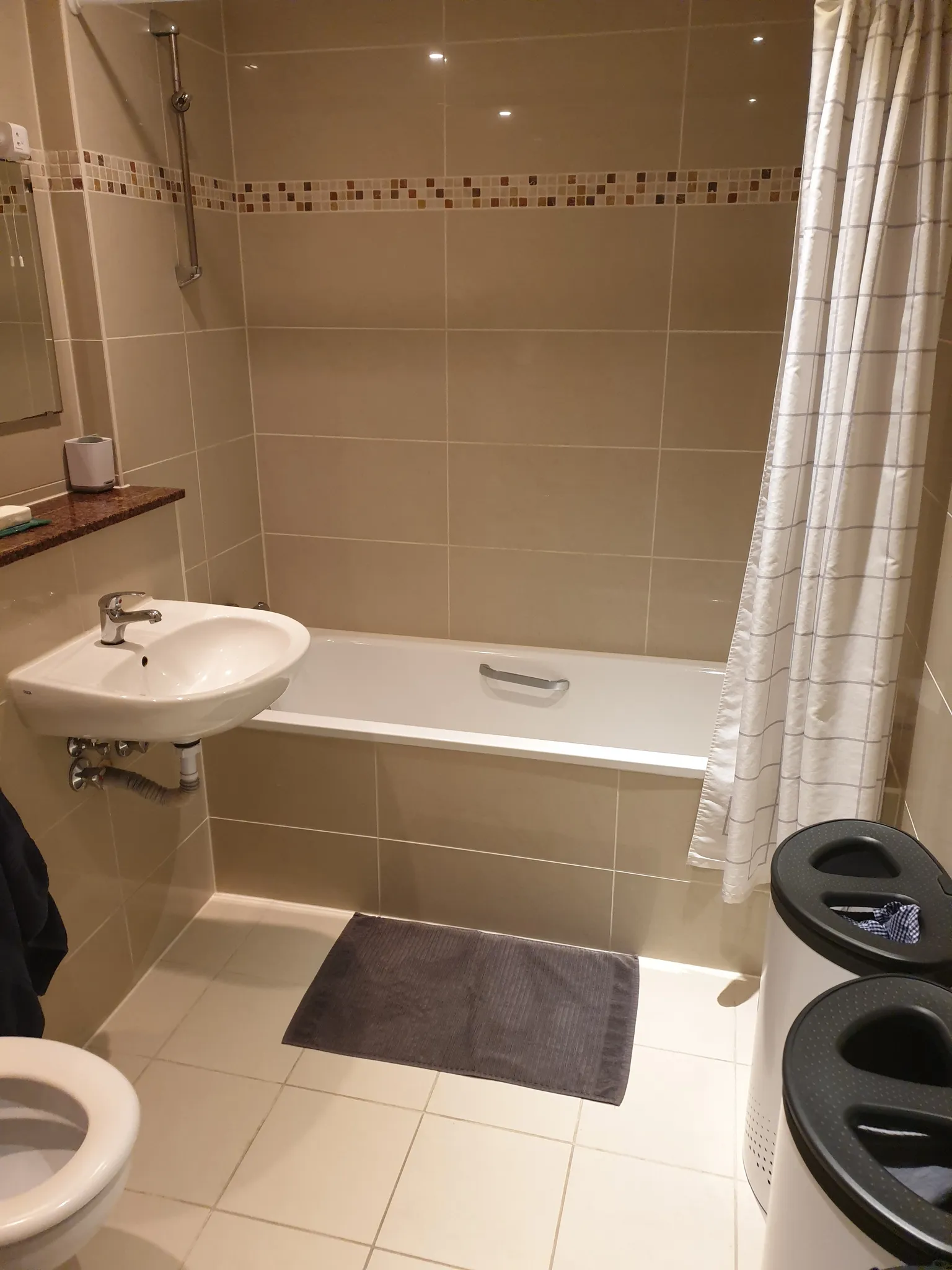 Bathroom with a bathtub and overhead shower, wall-mounted sink, tiled walls, and a shower curtain