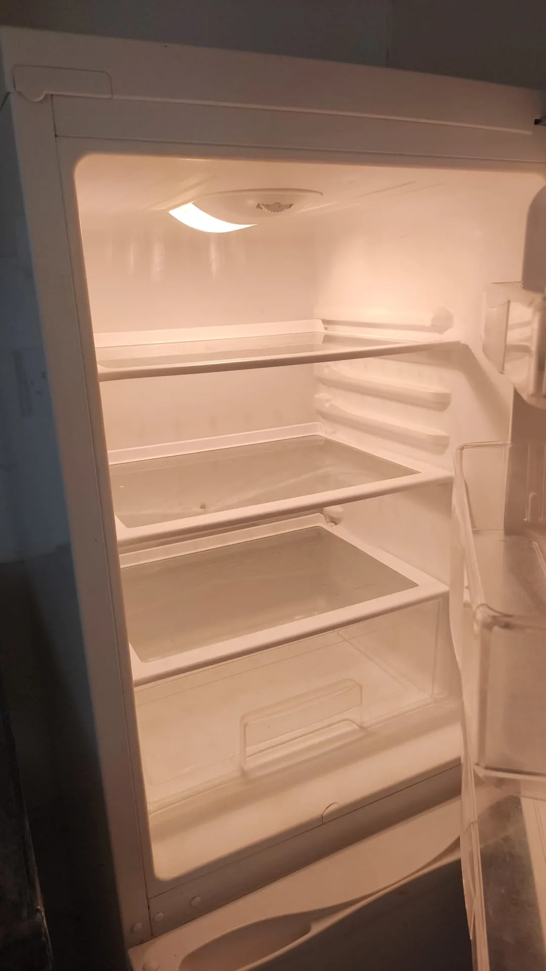 Interior of an empty refrigerator with multiple glass shelves, a bottom drawer, interior light, and the door partially open.