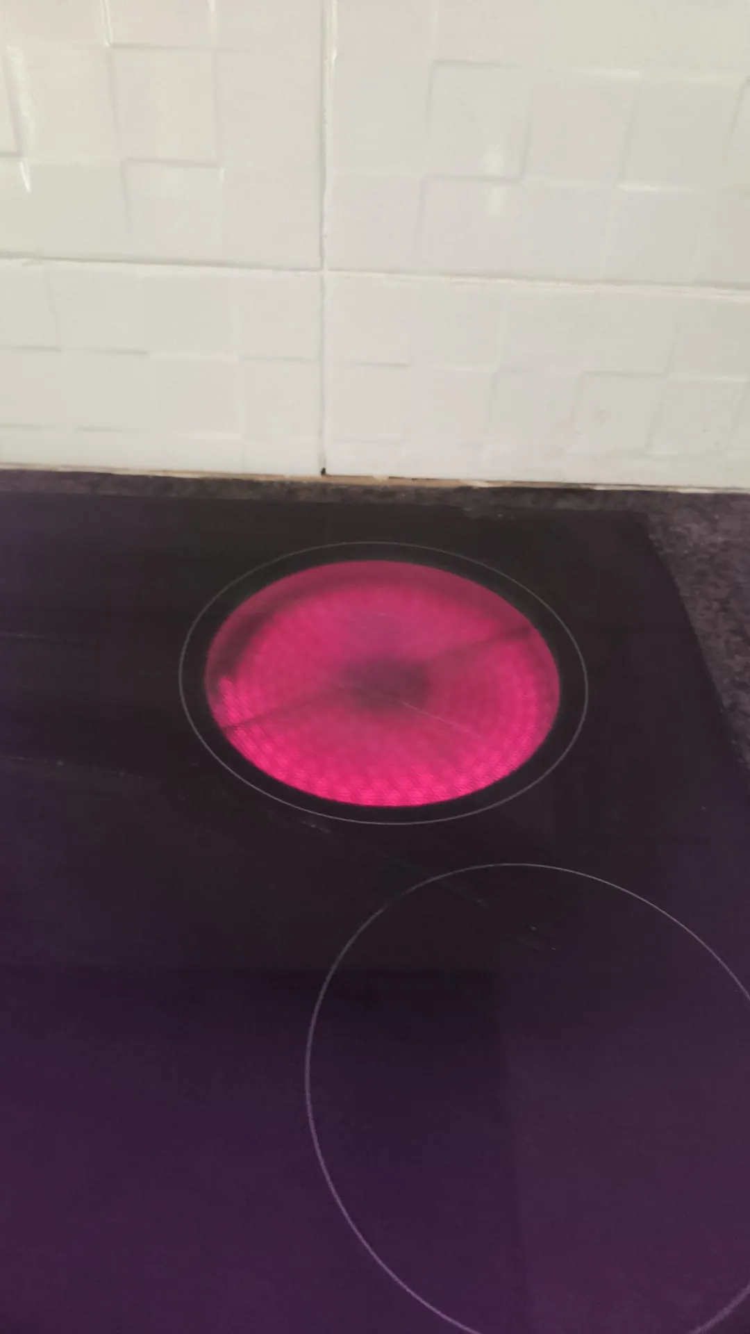 Kitchen electric cooktop with one glowing red heating element and white tiled backsplash.