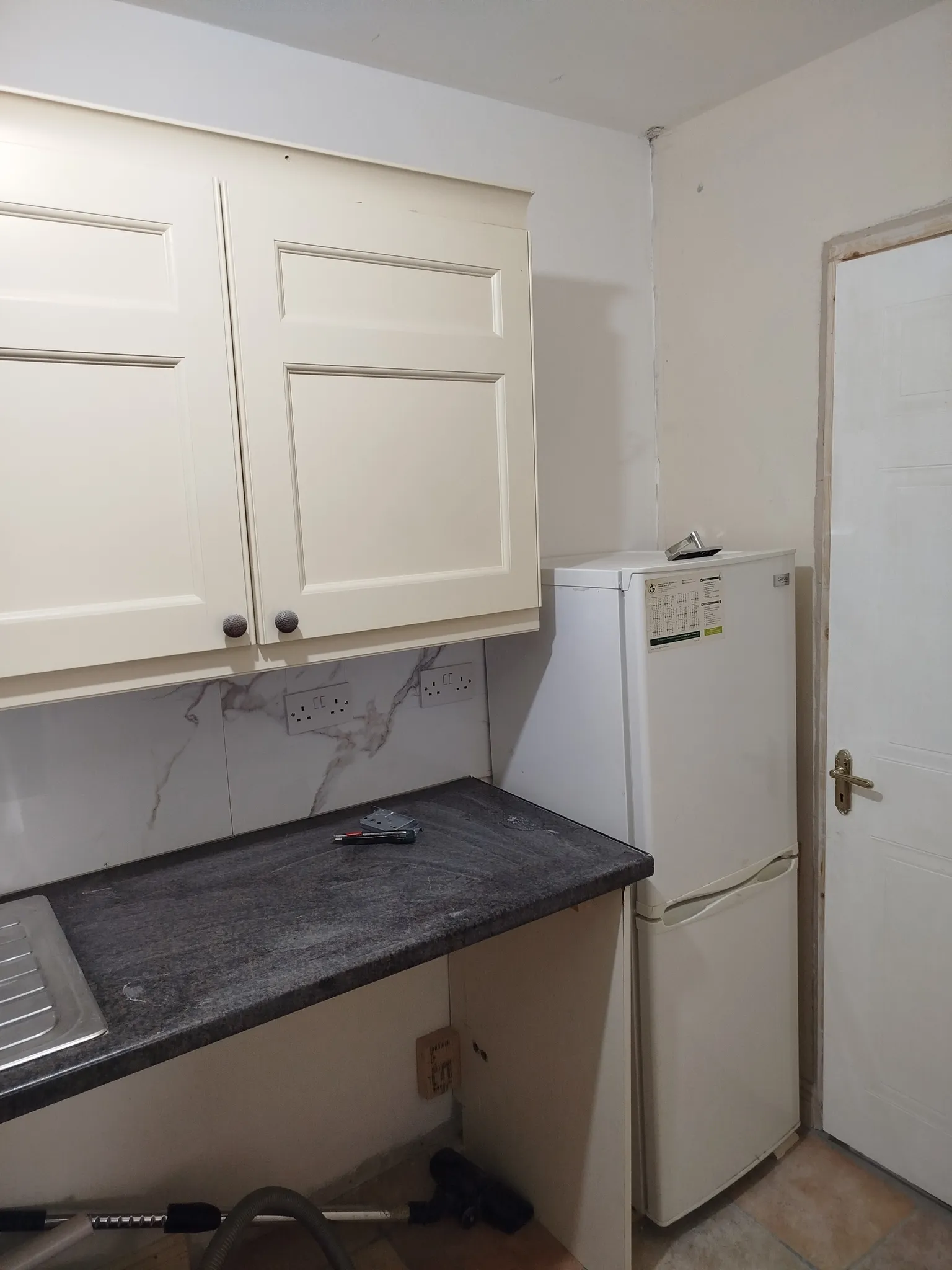 Kitchen corner with upper cabinets, dark countertop, small freestanding refrigerator and a closed door.