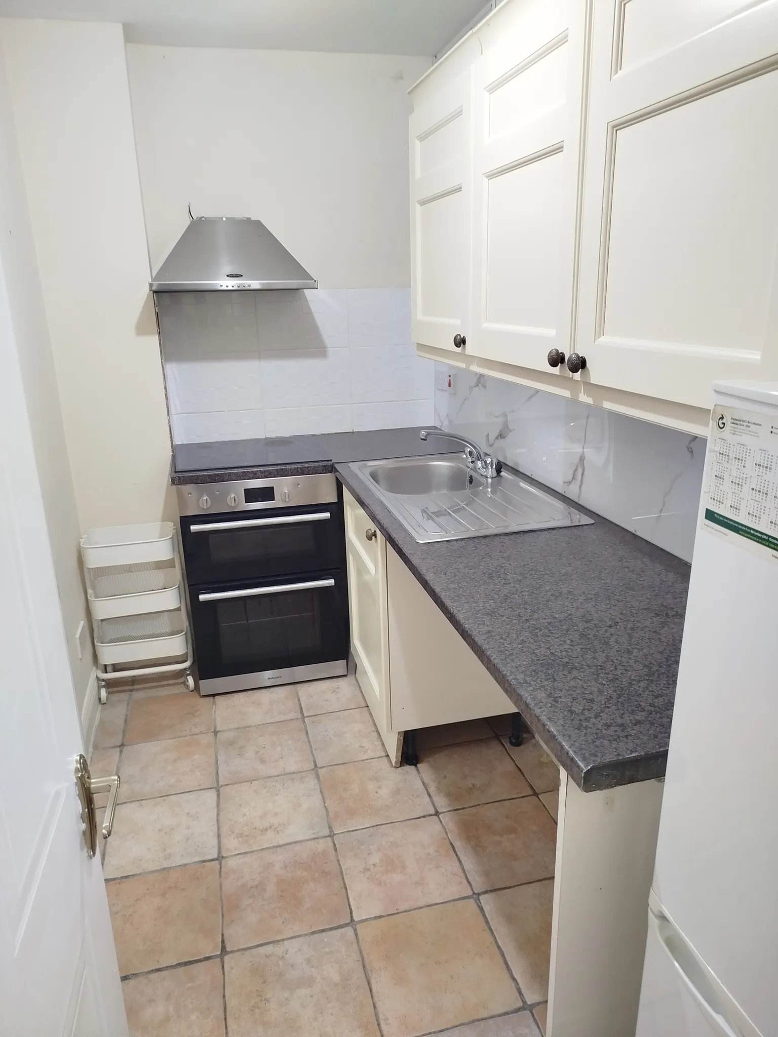 Small kitchen with a dark countertop, stainless steel sink, oven with extractor hood, and white upper cabinets.