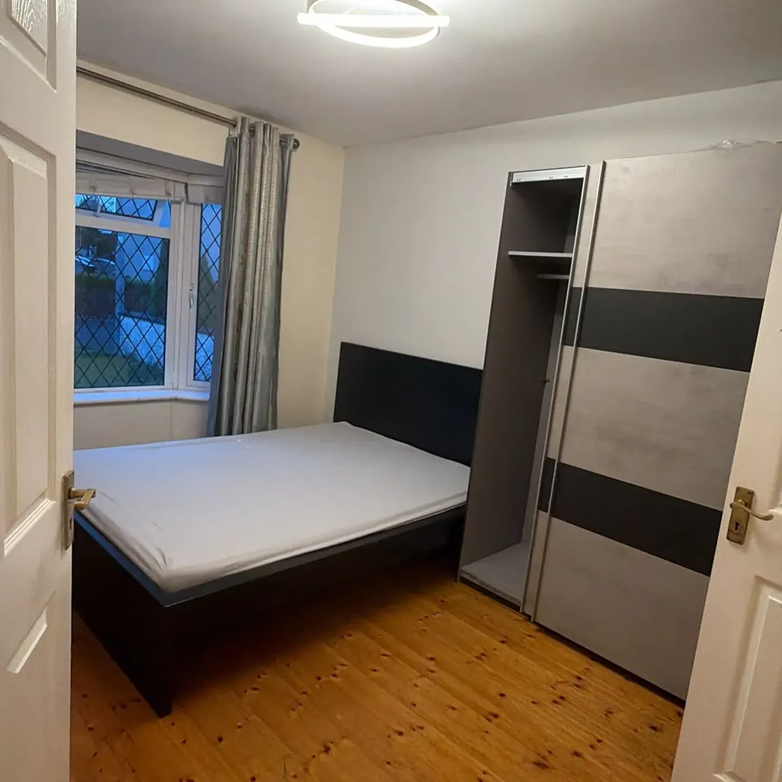 Bedroom with a double bed and mattress, a partially open wardrobe, a window with curtains, and a ceiling light.